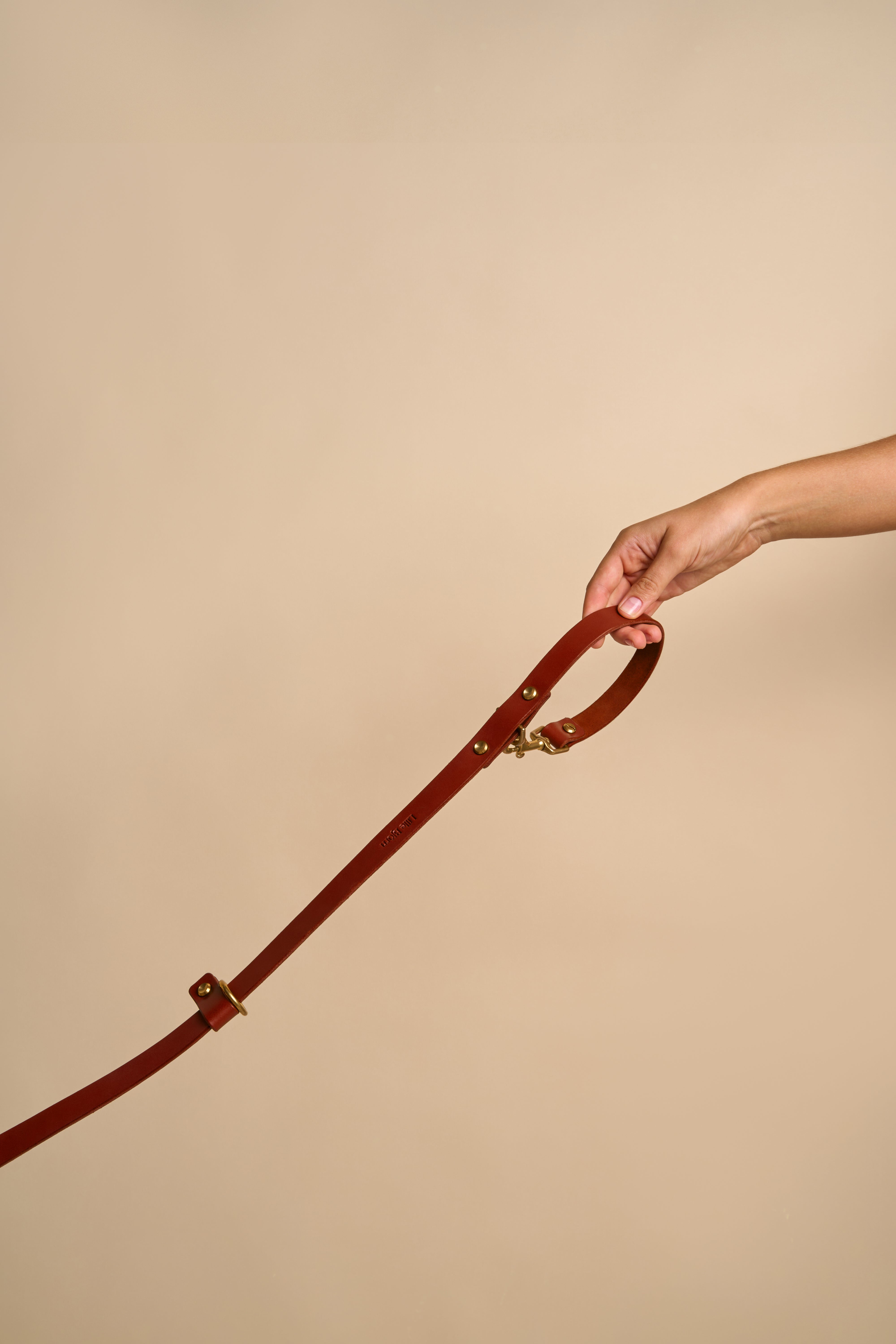 Omni Cognac Leather Dog Leash held in hand, showing versatile usage options and durable brass hardware